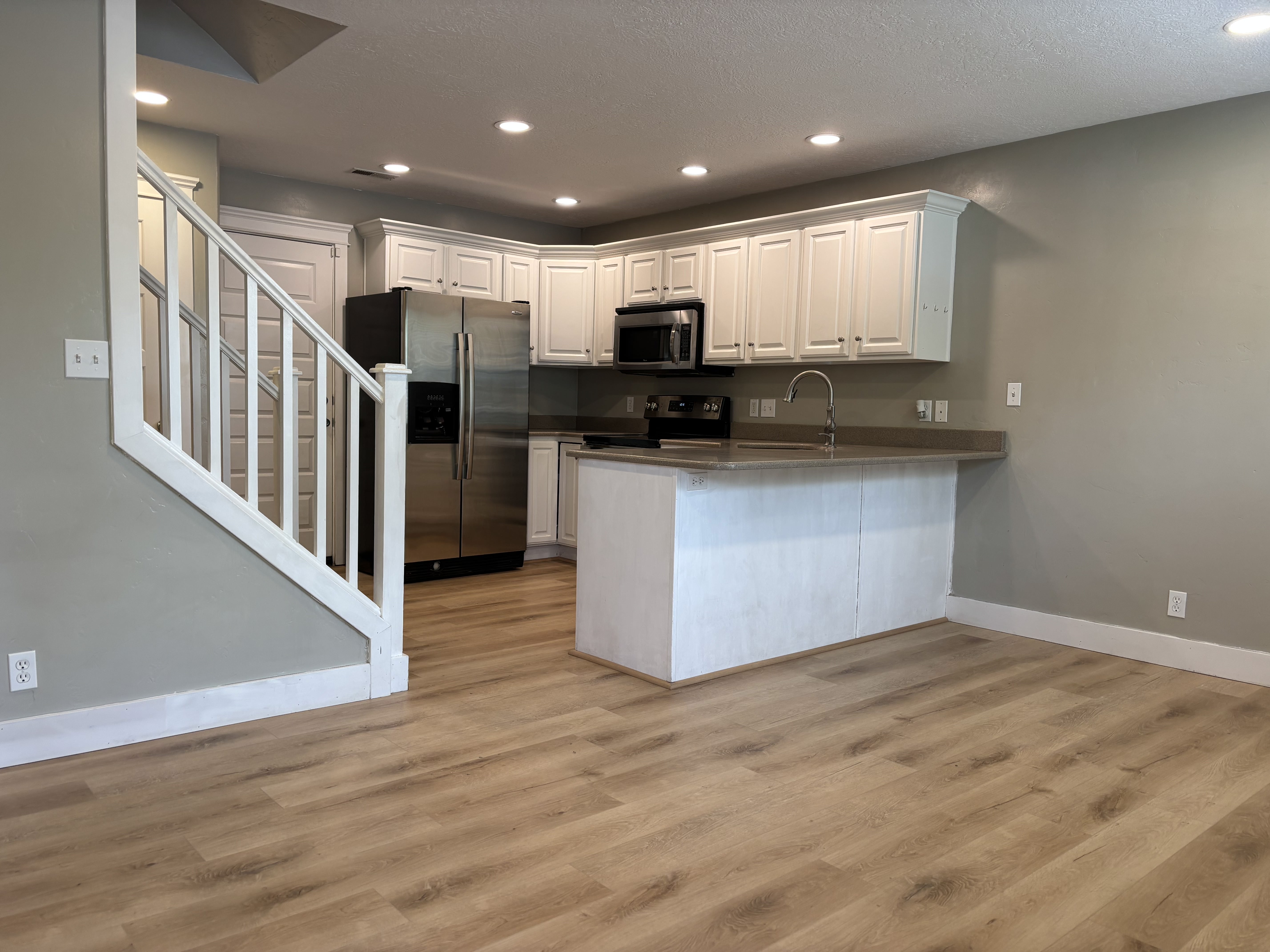 Open-concept kitchen featuring wood-finish flooring, white cabinetry, recessed lighting, stainless steel appliances, and a peninsula with a built-in sink
