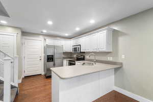 Kitchen with stainless steel appliances, light countertops, a peninsula, white cabinetry, and dark wood-type flooring
