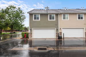 Back of house with roof with shingles, a garage, stone siding, and driveway