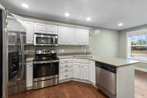 Kitchen with stainless steel appliances, a peninsula, dark wood-type flooring, white cabinets, and recessed lighting