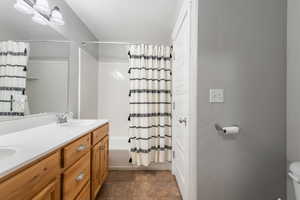 Bathroom with double vanity, shower / bath combination with curtain, and a textured ceiling