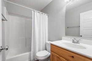 Bathroom with a textured ceiling, vanity, and shower / bathtub combination with curtain