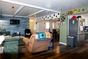 Living room with an accent wall, beam ceiling, and dark wood-style floors