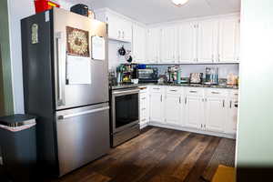 Kitchen with stainless steel appliances, white cabinetry, dark wood-style floors, and dark stone counters