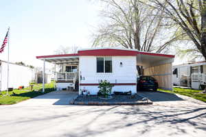 Manufactured / mobile home with concrete driveway, an attached carport, covered porch, and a front yard
