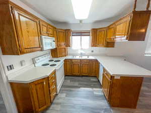 Kitchen featuring white appliances, wood finish cabinets, light countertops, and a peninsula