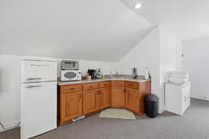 Studio apartment with bar and white appliances, vaulted ceiling, wood finish cabinets, light countertops, and light carpet