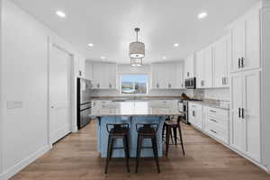 Dual tone kitchen featuring a breakfast bar, a center island, light stone countertops, stainless steel appliances, and hanging light fixtures