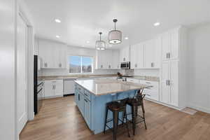 Kitchen featuring a kitchen breakfast bar, hanging light fixtures, two tone cabinets, a center island, and light stone counters