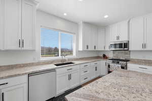 Kitchen with white cabinetry, stainless steel appliances, light stone countertops, and recessed lighting