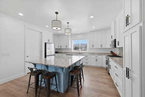 Dual tone kitchen with a kitchen island, a breakfast bar, light stone counters, hanging light fixtures, and stainless steel appliances