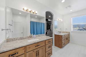 Primary bathroom with two vanities, curtained shower, light tile patterned flooring, and a walk in closet