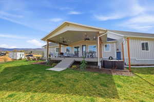 Rear view of property with covered deck, ceiling fan, board and batten siding, a yard, roof with shingles, with mountain view