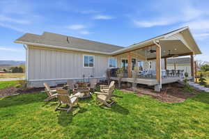 Rear view of house featuring ceiling fan, a fire pit, roof with shingles, a deck, and a lawn