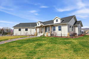 View of front facade featuring covered porch, board and batten siding, a shingled roof, and a front lawn
