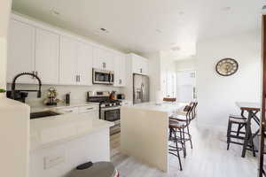 Kitchen with stainless steel appliances, a kitchen island, white cabinetry, light wood-style flooring, and a breakfast bar