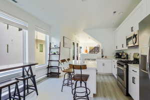 Kitchen featuring stainless steel appliances, white cabinetry, a kitchen bar, light wood-type flooring, and a center island