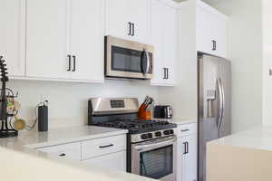 Kitchen with stainless steel appliances, white cabinets, and light stone countertops