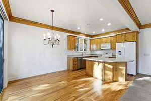 Kitchen with white appliances, suspended lighting, wood finish cabinetry, ornamental molding, and light wood-style floors