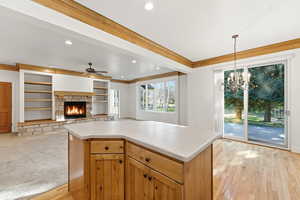 Kitchen featuring light countertops, ornamental molding, a stone fireplace, open floor plan, and light wood-style flooring