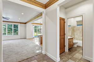 Hall with ornamental molding, light carpet, light stone finish flooring, and a chandelier