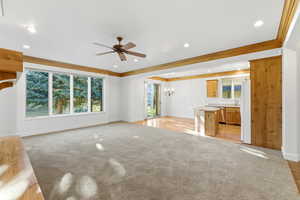 Unfurnished living room featuring ceiling fan, hanging lights, light carpet, and ornamental molding