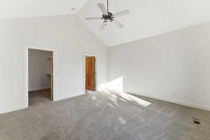 Unfurnished bedroom with a high ceiling, a walk in closet, light colored carpet, and a ceiling fan