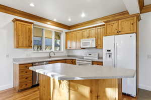 Kitchen with white appliances, a center island, crown molding, light wood-style floors, and recessed lighting