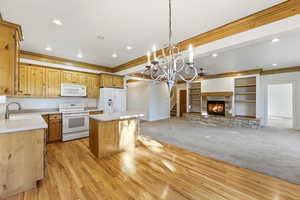 Kitchen featuring a kitchen island, open floor plan, white appliances, suspended lighting, and a fireplace