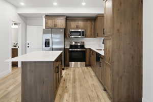 Kitchen with stainless steel appliances, a kitchen island, light wood finished floors, recessed lighting, and light stone counters