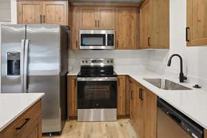Kitchen with stainless steel appliances, light wood finished floors, wood finish cabinetry, and light stone countertops
