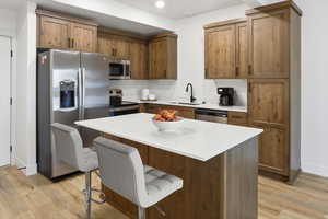 Kitchen with stainless steel appliances, a center island, a breakfast bar, light wood finished floors, and wood finish cabinetry