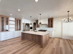 Two tone kitchen with glass fronted cabinets, open shelves, arched walkways, stainless steel appliances, and a kitchen island with sink