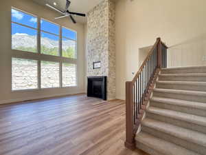 Unfurnished living room with a high ceiling, light wood-style floors, a mountain view, a ceiling fan, and a stone fireplace