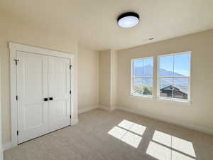 Unfurnished bedroom with a mountain view, light colored carpet, and a closet