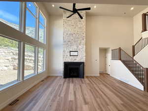 Unfurnished living room featuring a fireplace, a high ceiling, light wood-type flooring, a ceiling fan, and recessed lighting