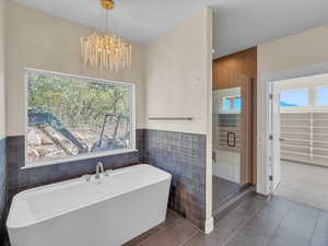 Full bathroom featuring a soaking tub, a shower stall, a chandelier, tile walls, and dark tile patterned flooring