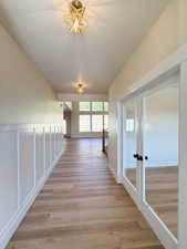 Corridor featuring french doors, light wood-type flooring, a textured ceiling, and a decorative wall