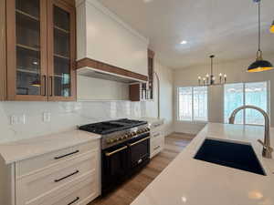 Kitchen with double oven range, glass fronted cabinets, light stone counters, light wood finished floors, and suspended lighting