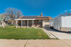 View of front of house with brick siding, roof mounted solar panels, an attached garage, a front lawn, and a porch