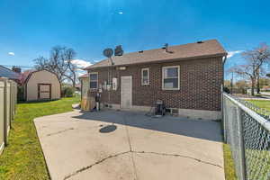 Back of property with a fenced backyard, a patio, brick siding, roof with shingles, and a storage unit