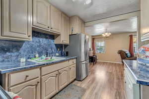 Kitchen featuring light wood finished floors, light wood finish cabinetry, suspended lighting, freestanding refrigerator, and a textured ceiling