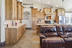 Kitchen with light stone countertops, decorative backsplash, stainless steel fridge with ice dispenser, gas stove, and lofted ceiling