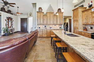 Kitchen featuring backsplash, a breakfast bar area, ceiling fan, light stone countertops, and pendant lighting