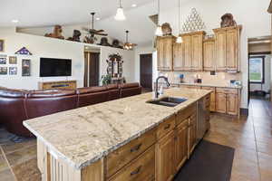 Kitchen with open floor plan, an island with sink, light stone counters, a ceiling fan, and lofted ceiling