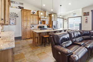 Kitchen with wood finish cabinetry, light stone countertops, vaulted ceiling, a kitchen breakfast bar, and a large island