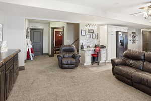 Living room with light colored carpet, ceiling fan, and a desk