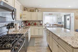 Kitchen with stainless steel appliances, cream cabinets, light stone countertops, light wood-style flooring, and a center island