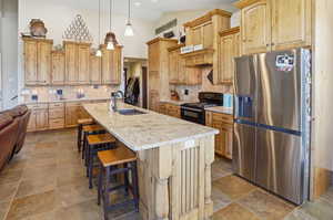 Kitchen featuring tasteful backsplash, stainless steel fridge with ice dispenser, black gas range, lofted ceiling, and a kitchen island with sink