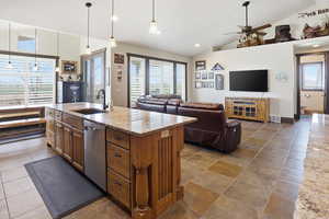 Kitchen with light stone counters, decorative light fixtures, open floor plan, a center island with sink, and wood finish cabinetry